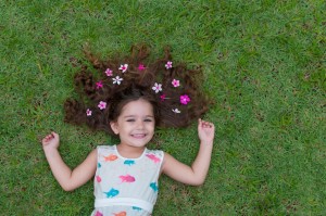 Beautiful and happy girl playing in the park, with wonderful lawn and flowers