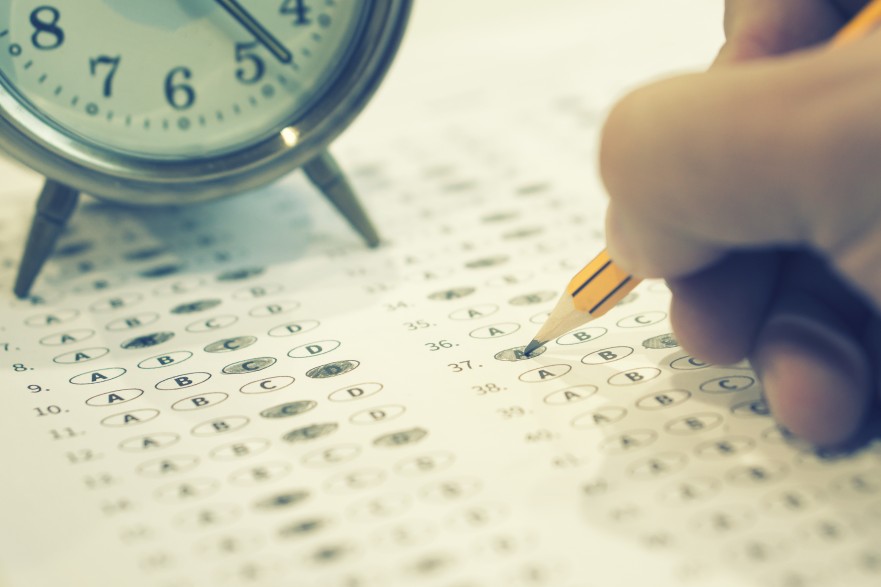 Student taking a standardized bubble in test with a clock nearby.